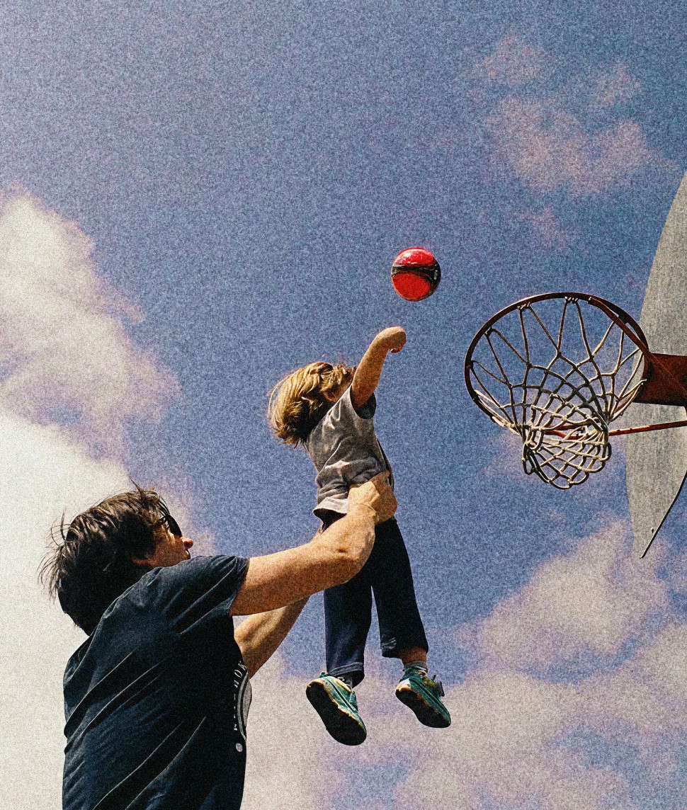 Child throwing a basketball at the hoop with some help